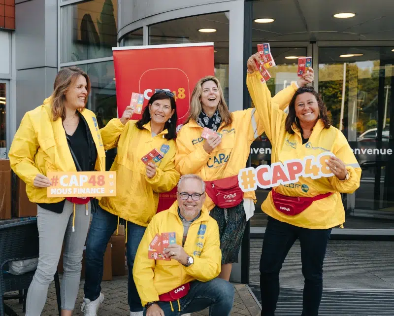 Cinq bénévoles CAP48 (quatre femmes et un homme) sourians devant un centre commercial.