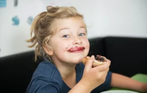 Un enfant avec une tartine en main et de la confiture autour de la bouche